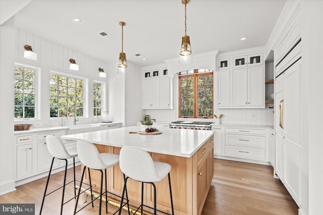 kitchen with visible vents, light wood-style flooring, glass insert cabinets, a kitchen bar, and a center island