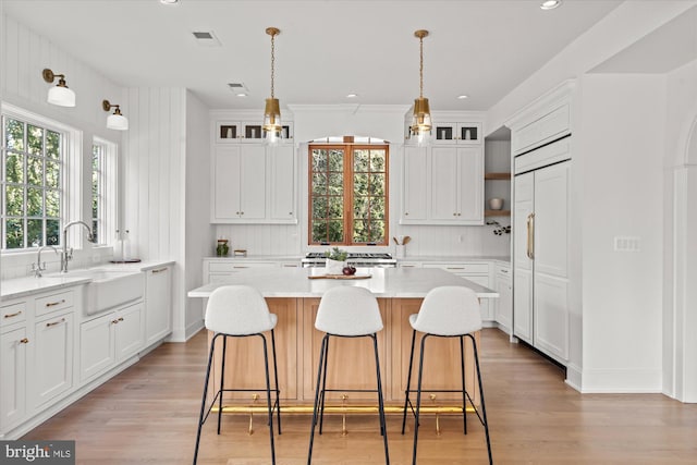 kitchen featuring white cabinets, a center island, light wood-style floors, and a sink