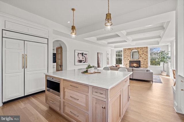 kitchen featuring paneled refrigerator, coffered ceiling, a stone fireplace, and light wood-style flooring