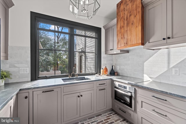 kitchen with brick floor, a sink, stainless steel oven, black electric stovetop, and tasteful backsplash