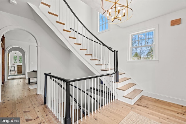 staircase featuring arched walkways, a healthy amount of sunlight, and hardwood / wood-style flooring