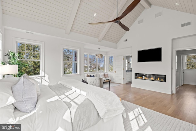 bedroom with a glass covered fireplace, beam ceiling, wood finished floors, and visible vents