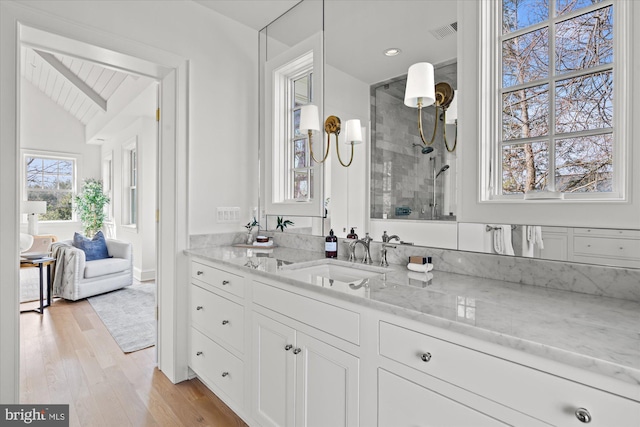 full bath featuring vanity, wood finished floors, visible vents, tiled shower, and vaulted ceiling