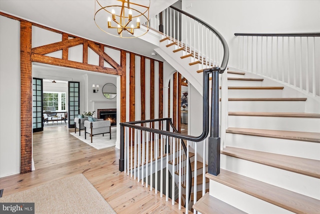 staircase with a notable chandelier, a warm lit fireplace, and wood finished floors