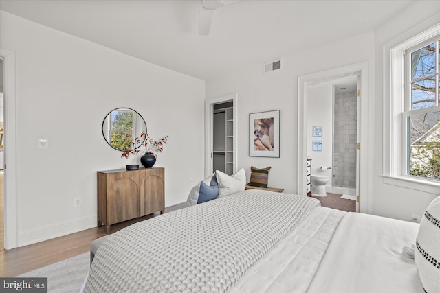 bedroom with wood finished floors, visible vents, baseboards, ensuite bathroom, and a walk in closet