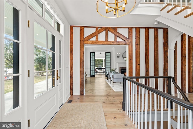 entrance foyer featuring an inviting chandelier, stairway, light wood-style floors, and a warm lit fireplace