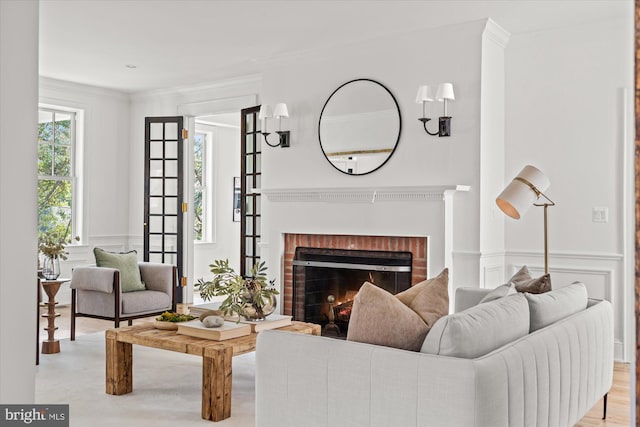 living room with light wood-style flooring, ornamental molding, wainscoting, a decorative wall, and a brick fireplace