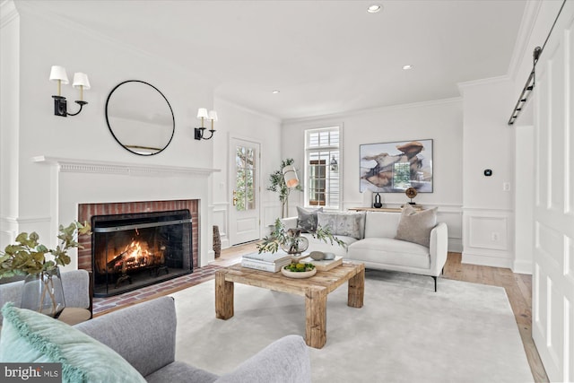 living area featuring wood finished floors, a decorative wall, wainscoting, crown molding, and a brick fireplace