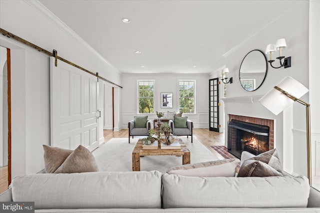 living area with ornamental molding, wood finished floors, recessed lighting, a barn door, and a brick fireplace