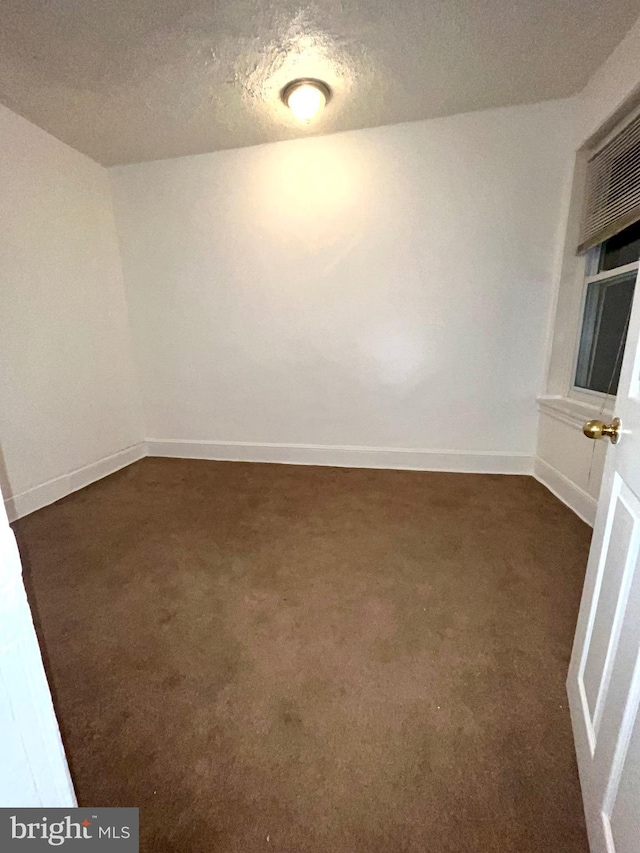 spare room featuring a textured ceiling and dark colored carpet