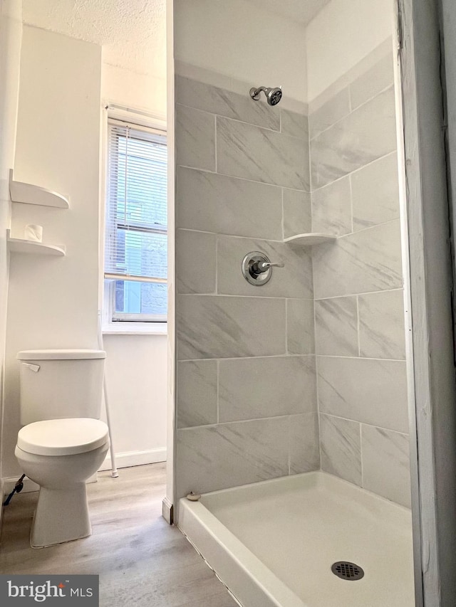 bathroom featuring hardwood / wood-style flooring, tiled shower, and toilet