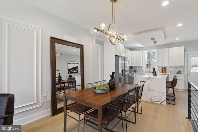 dining area with an inviting chandelier, sink, and light hardwood / wood-style floors