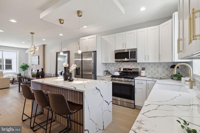 kitchen featuring sink, appliances with stainless steel finishes, a center island, light stone counters, and white cabinets