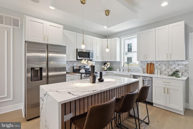 kitchen with a raised ceiling, a kitchen island, pendant lighting, stainless steel appliances, and white cabinets