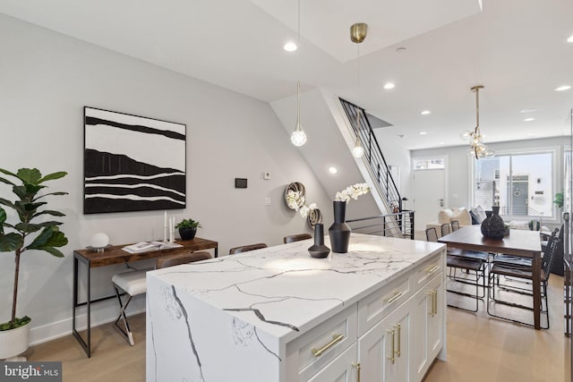 kitchen with pendant lighting, light hardwood / wood-style flooring, light stone countertops, white cabinets, and a kitchen island