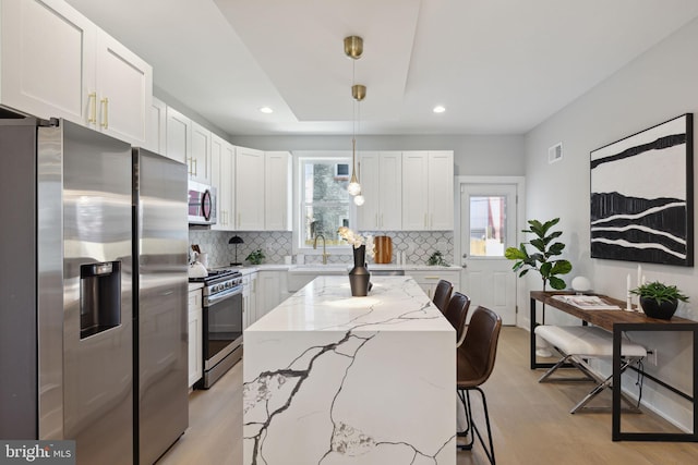 kitchen with pendant lighting, white cabinetry, stainless steel appliances, and a kitchen breakfast bar