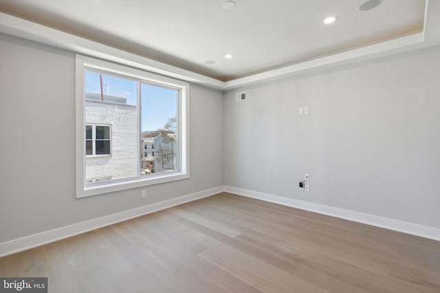 empty room with a tray ceiling and light hardwood / wood-style floors