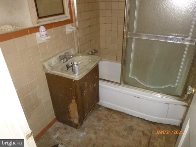 bathroom featuring sink, combined bath / shower with glass door, and tile walls