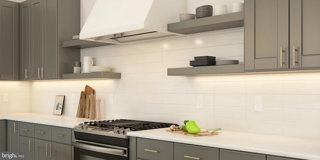 kitchen featuring decorative backsplash, stainless steel range with gas stovetop, custom range hood, and gray cabinetry