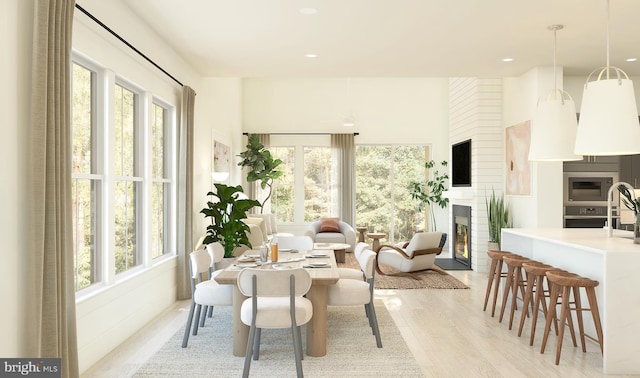 dining space featuring a large fireplace, a healthy amount of sunlight, and light wood-type flooring