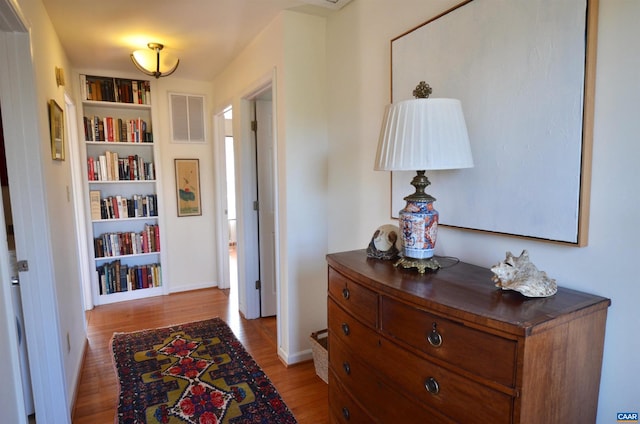 hall with built in shelves and light wood-type flooring