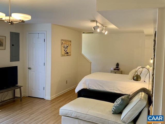 bedroom featuring electric panel, ceiling fan with notable chandelier, and light wood-type flooring