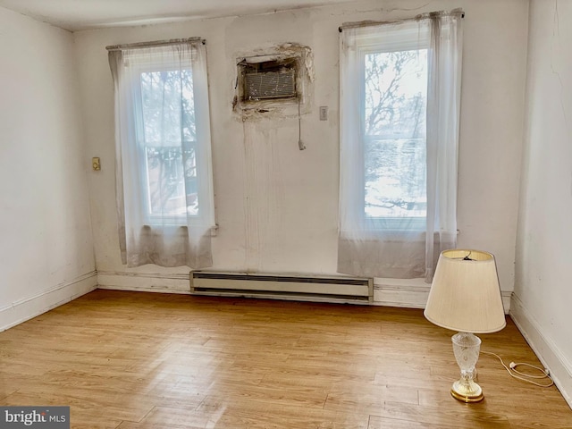 unfurnished room featuring a baseboard radiator, an AC wall unit, and light wood-type flooring