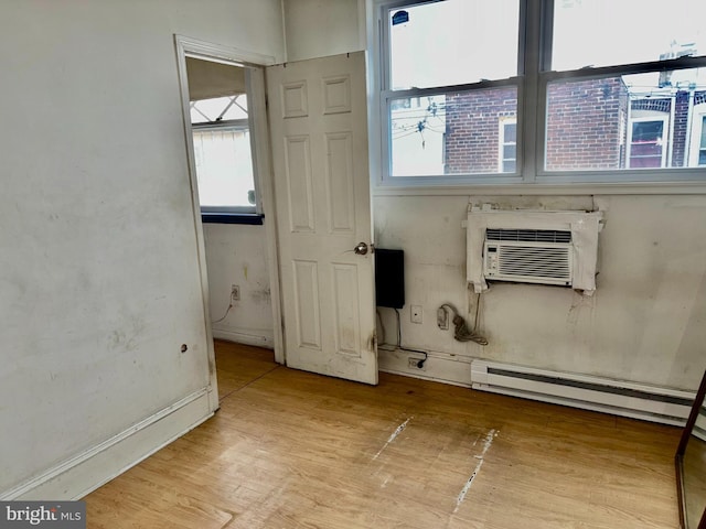 empty room with a baseboard radiator, an AC wall unit, and light wood-type flooring