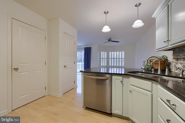 kitchen featuring sink, dark stone countertops, decorative light fixtures, stainless steel dishwasher, and light wood-type flooring