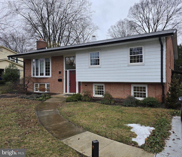 bi-level home featuring a front yard, a chimney, and brick siding