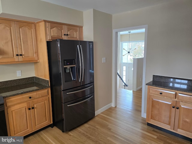 kitchen with dark stone counters, refrigerator with ice dispenser, and light hardwood / wood-style flooring