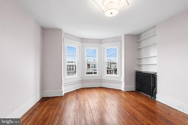 empty room with dark wood-type flooring, radiator, and built in features