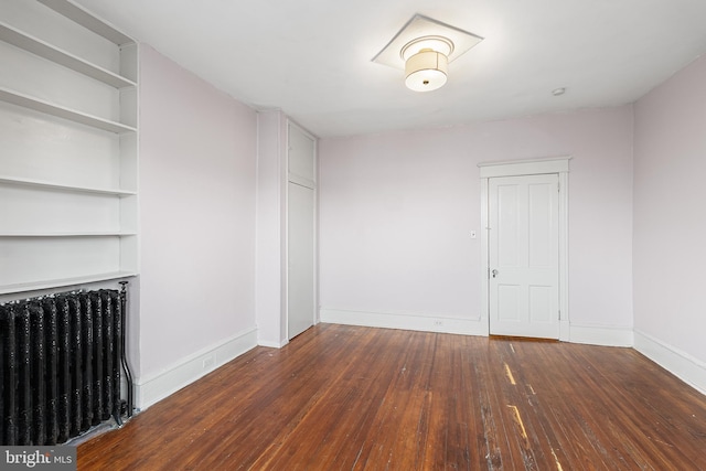 unfurnished room featuring built in shelves, radiator heating unit, and dark hardwood / wood-style flooring