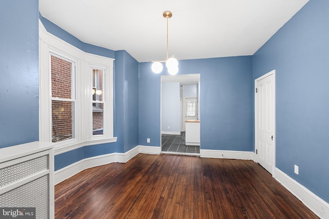 empty room with dark hardwood / wood-style floors and an inviting chandelier