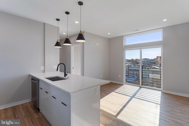 kitchen with white cabinetry, an island with sink, sink, hanging light fixtures, and light stone counters