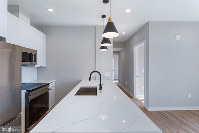 kitchen with white cabinetry, sink, hanging light fixtures, light stone counters, and stainless steel appliances