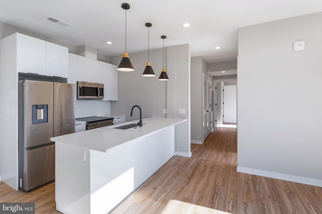 kitchen featuring sink, a kitchen island with sink, hanging light fixtures, stainless steel appliances, and white cabinets