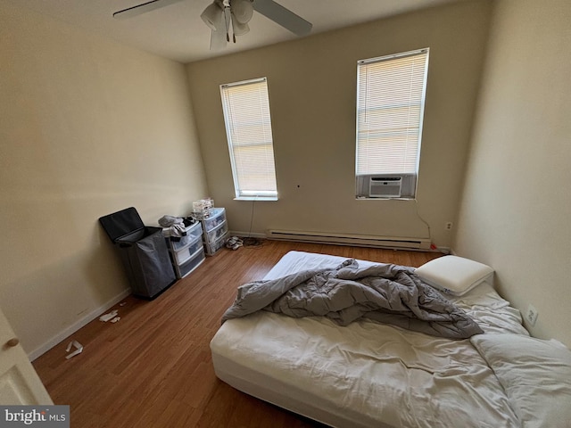 bedroom with multiple windows, a baseboard heating unit, cooling unit, and hardwood / wood-style floors