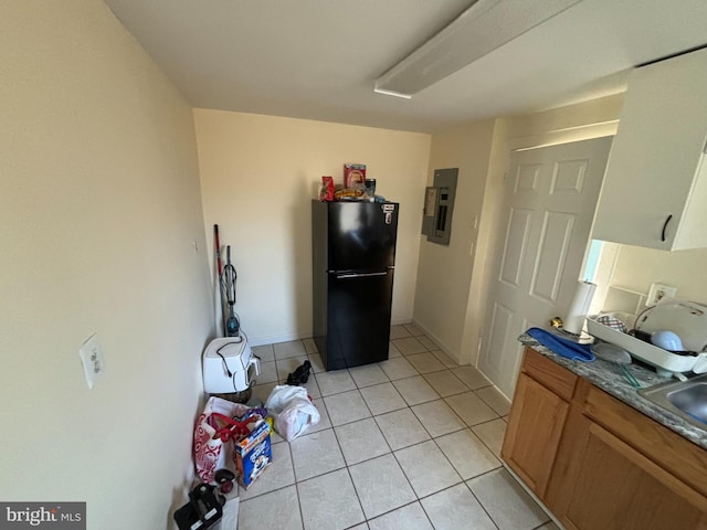 kitchen featuring black refrigerator, light tile patterned floors, and electric panel