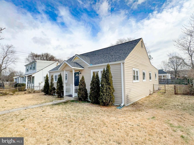 bungalow-style house featuring a shingled roof, fence, and a front lawn