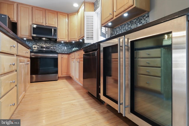 kitchen with stainless steel appliances, dark stone countertops, backsplash, and light hardwood / wood-style flooring