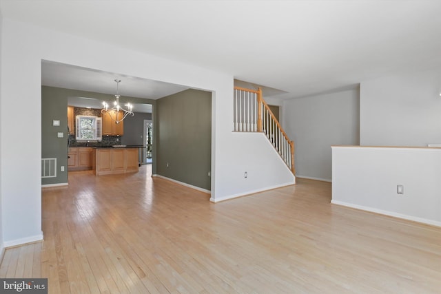 unfurnished living room with an inviting chandelier and light hardwood / wood-style flooring