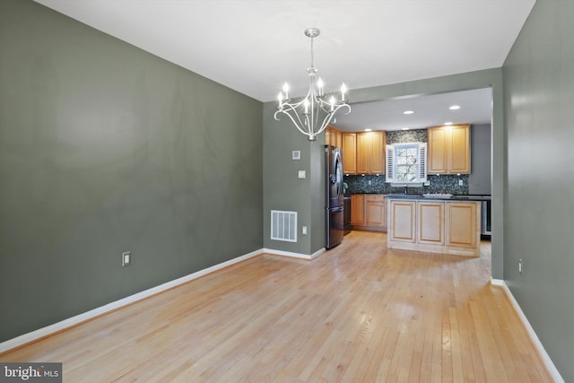 kitchen with decorative light fixtures, a chandelier, stainless steel fridge, light hardwood / wood-style floors, and decorative backsplash