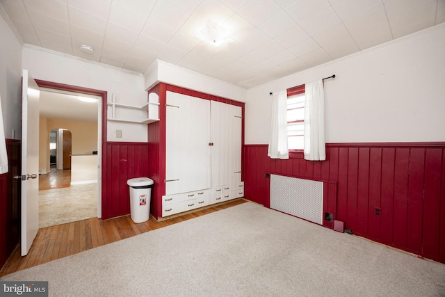 unfurnished bedroom featuring light hardwood / wood-style flooring, radiator heating unit, ornamental molding, and a closet