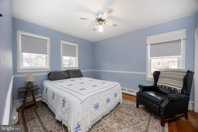 bedroom with ceiling fan, hardwood / wood-style floors, and a baseboard heating unit