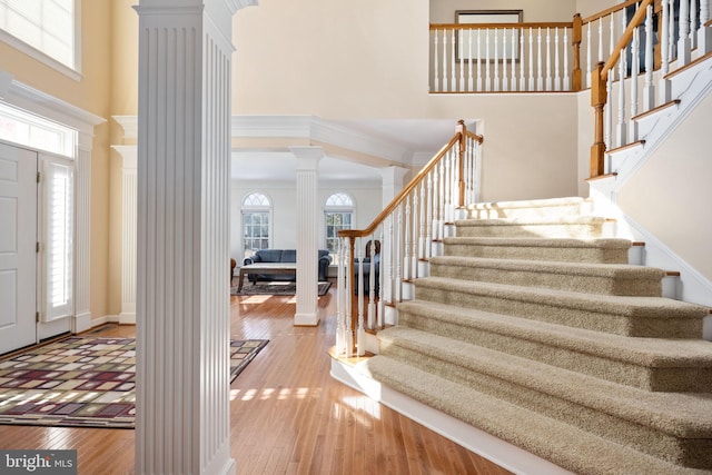 entryway with ornamental molding, decorative columns, hardwood / wood-style floors, and a high ceiling