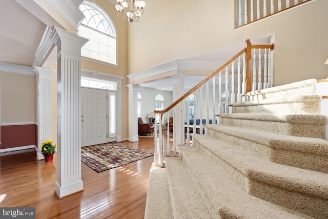 foyer entrance featuring crown molding, hardwood / wood-style floors, a towering ceiling, decorative columns, and a notable chandelier