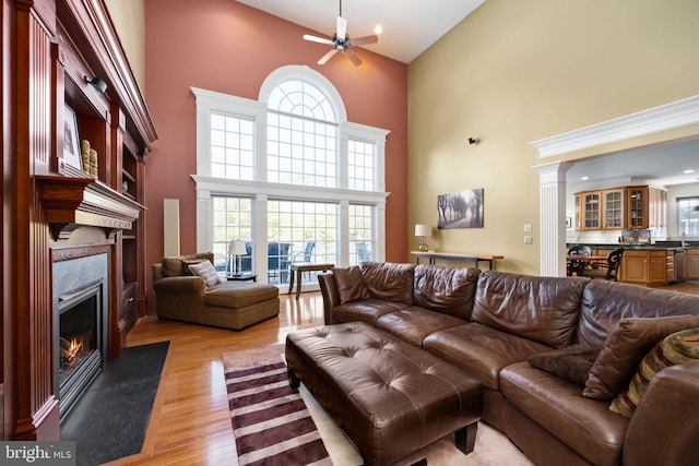 living room featuring light wood-type flooring, a high end fireplace, ceiling fan, and a high ceiling