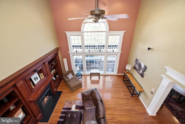 living room featuring ceiling fan, a towering ceiling, and light hardwood / wood-style floors