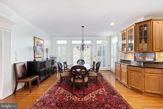 dining space featuring an inviting chandelier, ornate columns, and light wood-type flooring